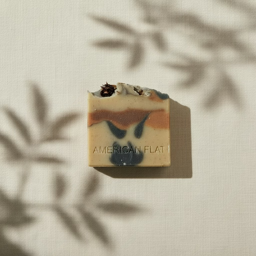 Tan colored soap with layers of charcoal and brown, topped with a miniature pinecone against a neutral background