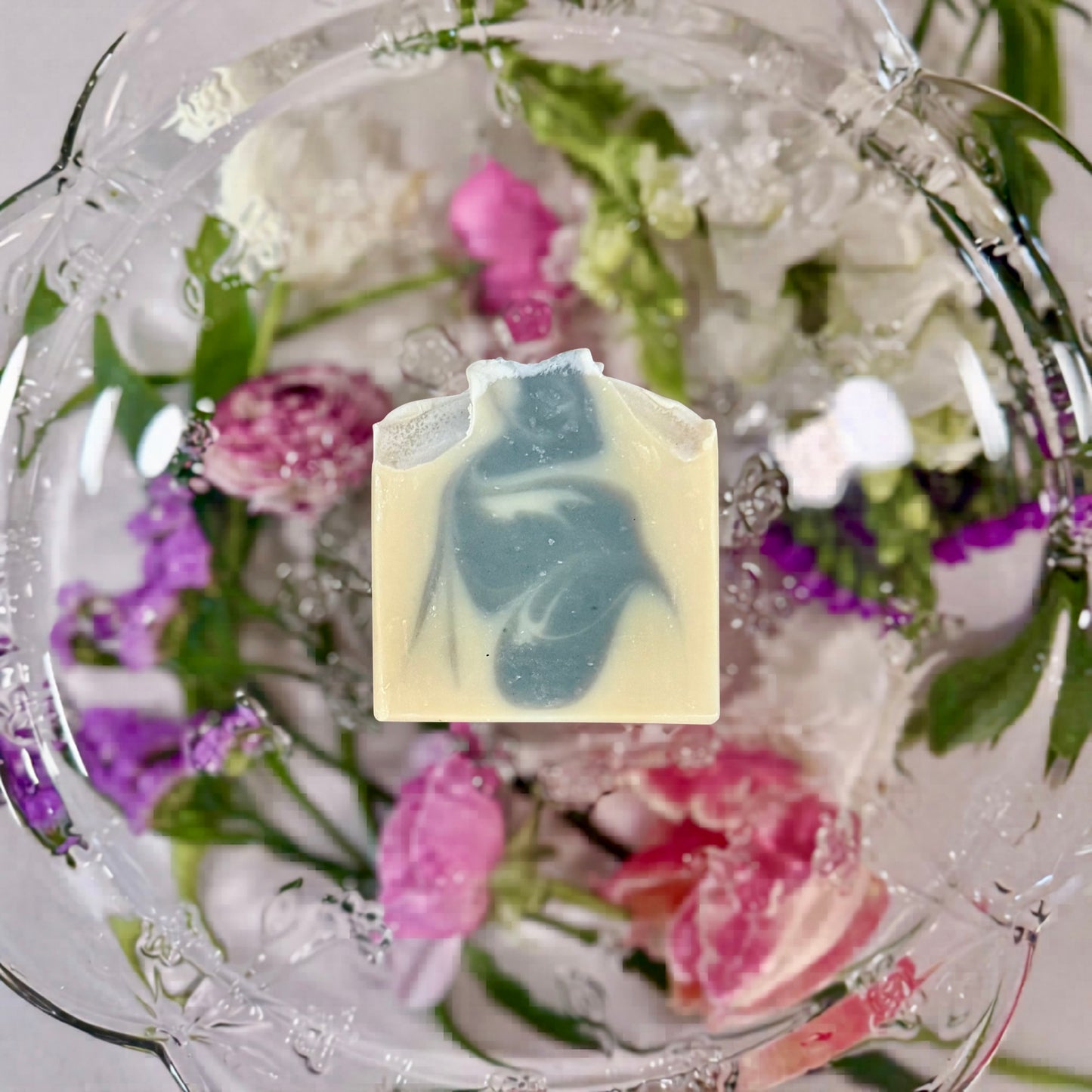 A WHITE AND BLUE SWIRLED BAR OF SOAP LAYING ON A GLASS PLATTER WITH DIFFERENT COLORED FLOWERS UNDERNEATH