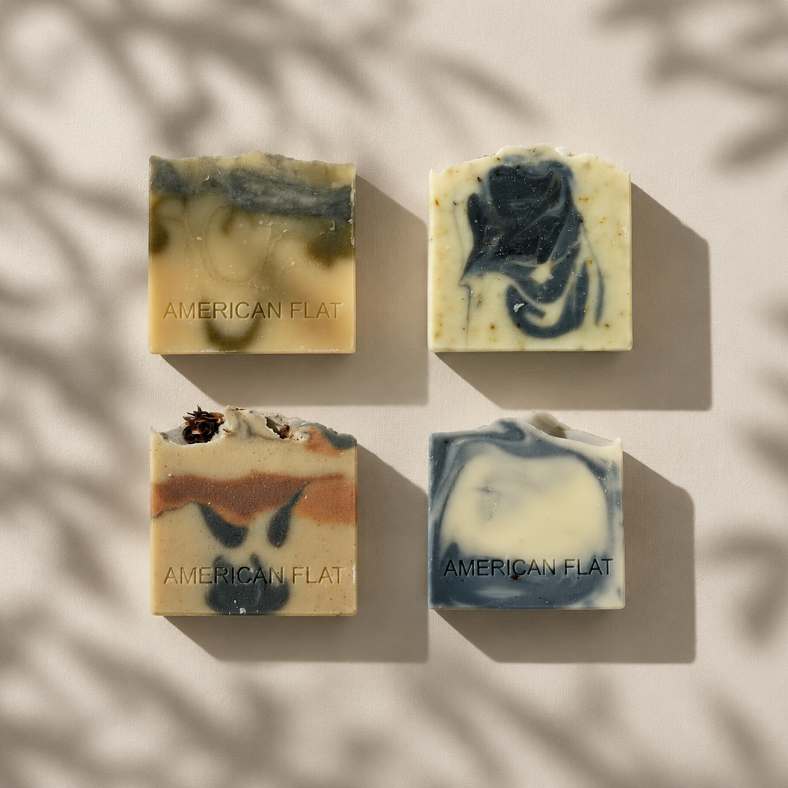 4 BARS OF SOAP SWIRLED WITH BLUE, CHARCOAL, GREEN AND BROWN CLAYS ON A NEUTRAL BACKGROUND WITH LIGHT SHADOWS