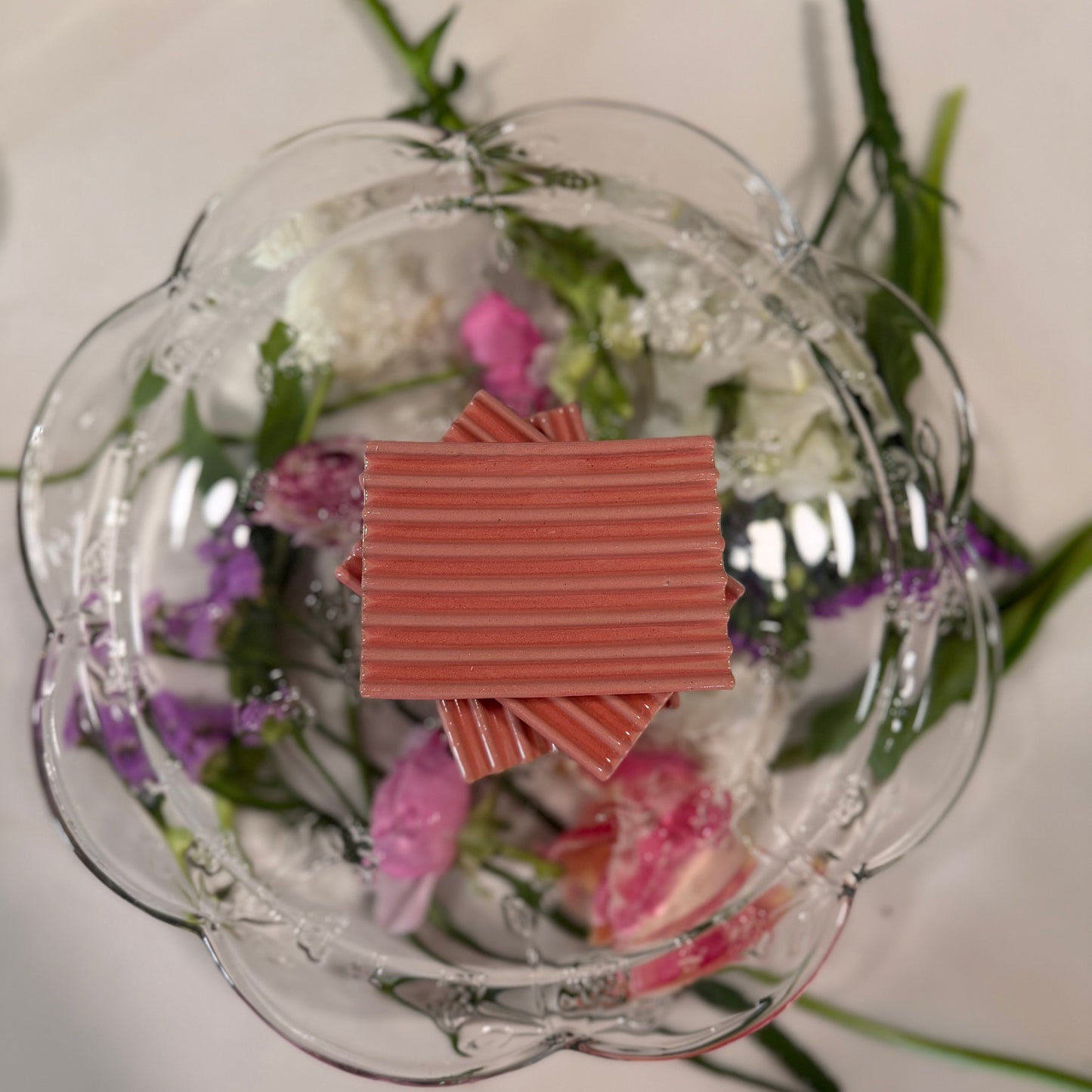 Decorative glass plate with flowers and a stack of 3 pink ceramic soap lifts on a white background