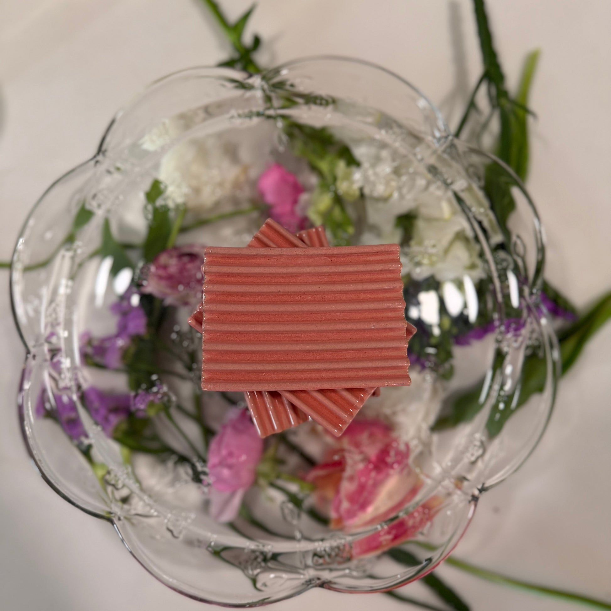 Decorative glass plate with flowers and a stack of 3 pink ceramic soap lifts on a white background