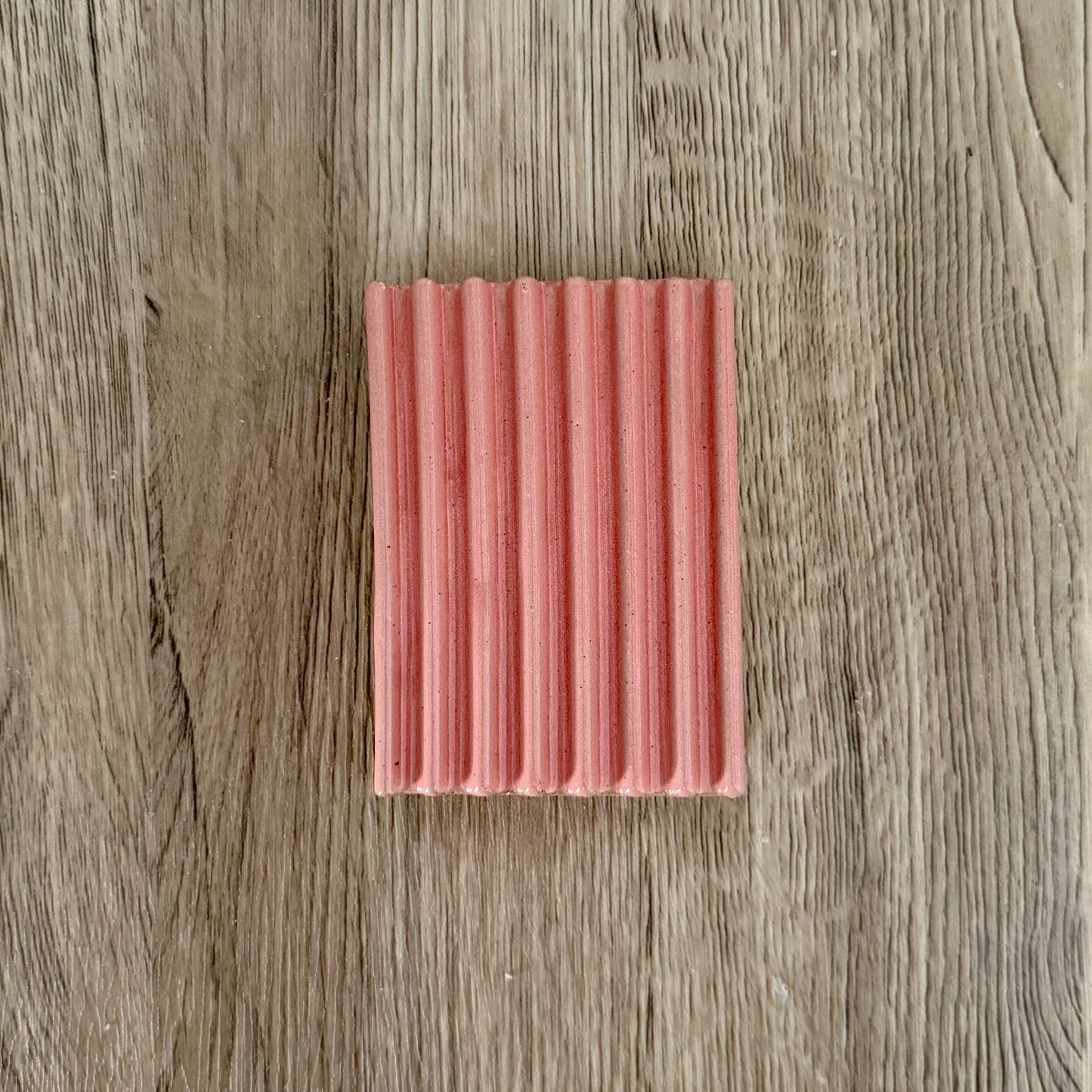 Rectangular pink ceramic soap lift with a ribbed texture on a wooden surface