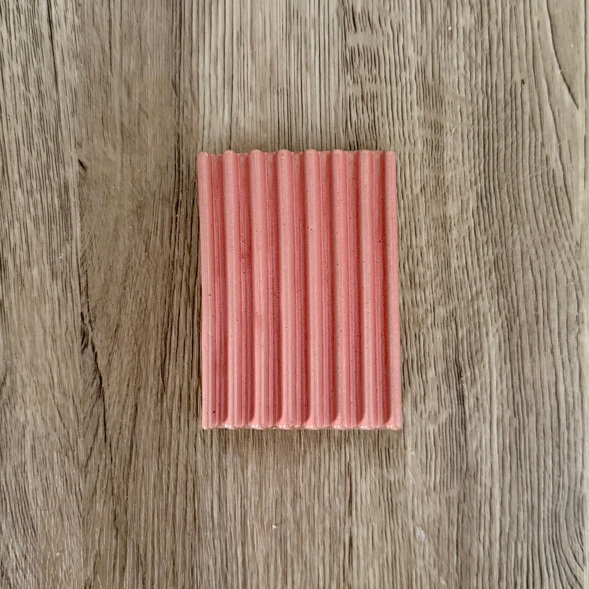 Rectangular pink ceramic soap lift with a ribbed texture on a wooden surface