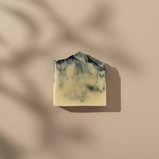 Cream bar of soap swirled on top with charcoal on a cream colored background with shadows