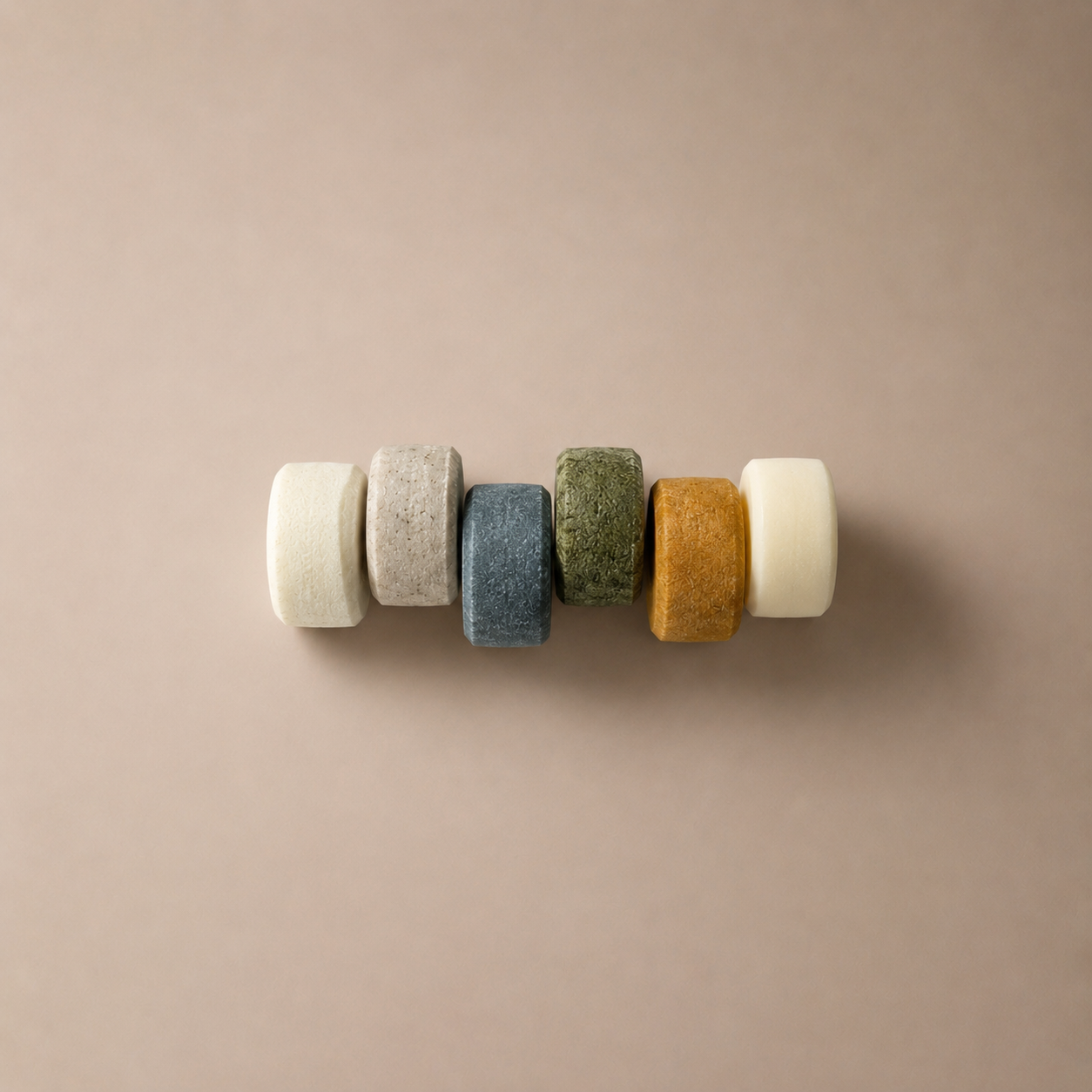 Set of six mini shampoo and conditioner bars in various colors on a beige background