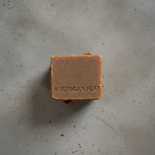 A square bar of soap stamped with American Flat soap ion a concrete backdrop.
