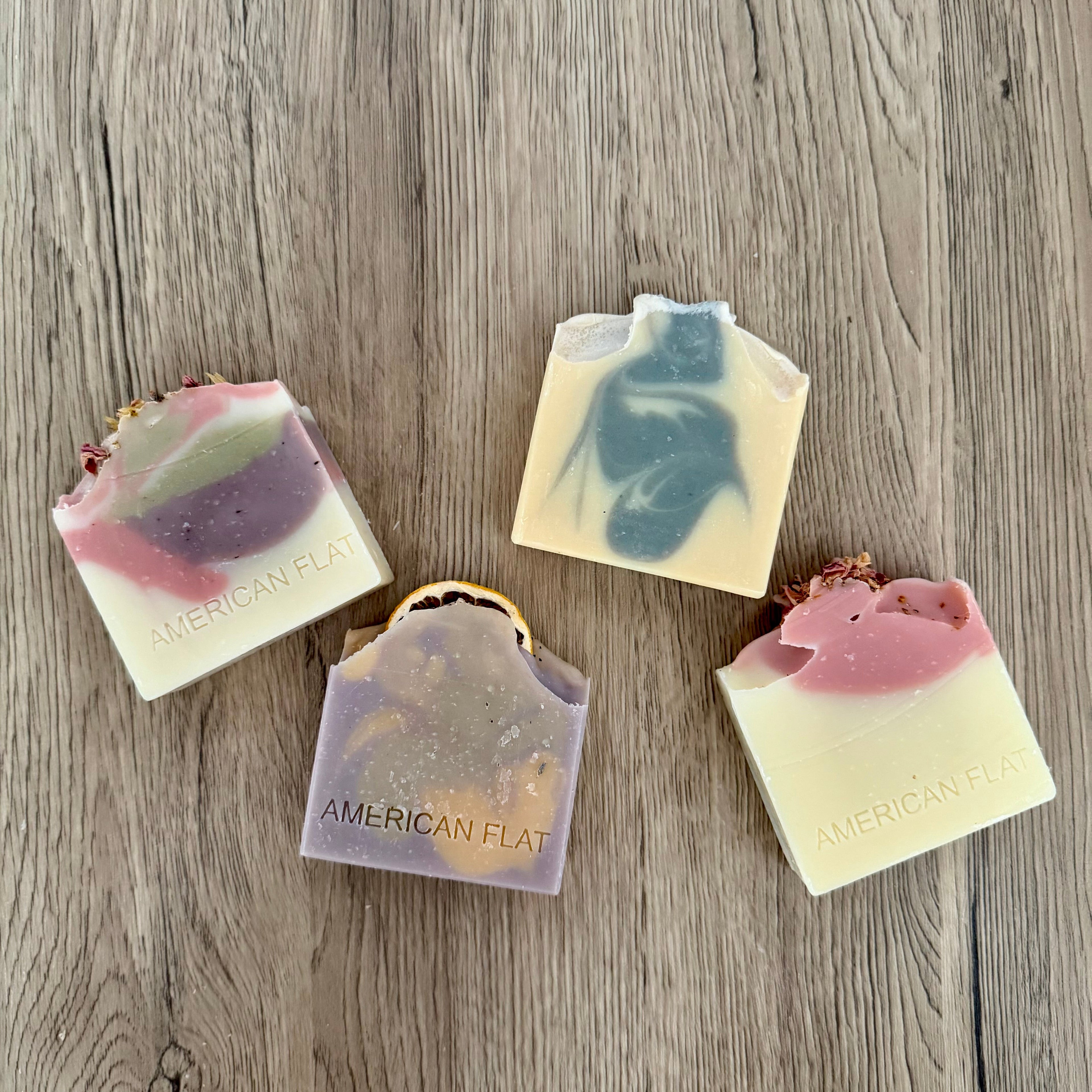 Four soap bars with different colors and designs on a wooden surface