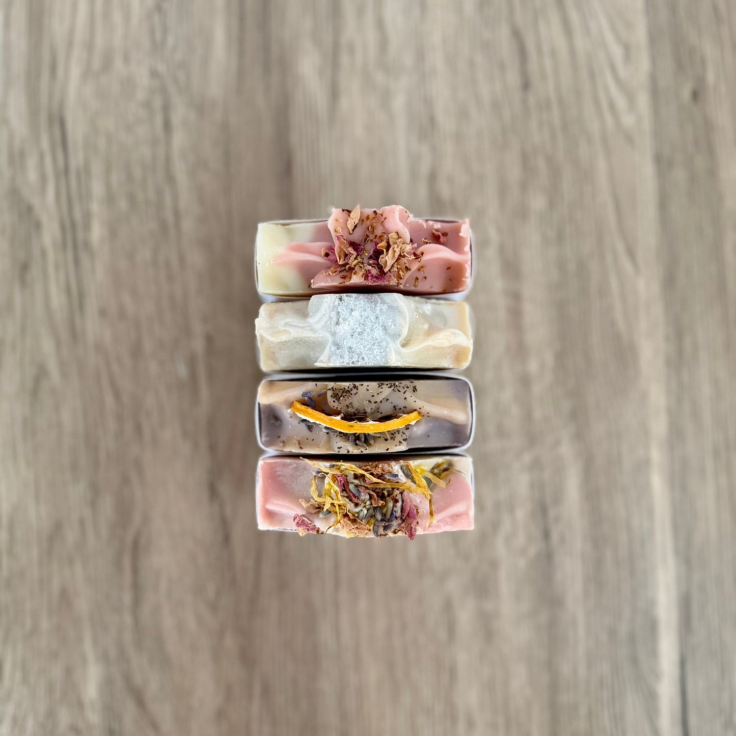 Stack of three soap bars with floral elements on a wooden surface