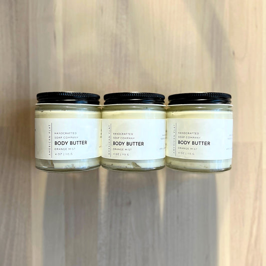 3 glass jars filled with whipped body butter on a natural wood surface